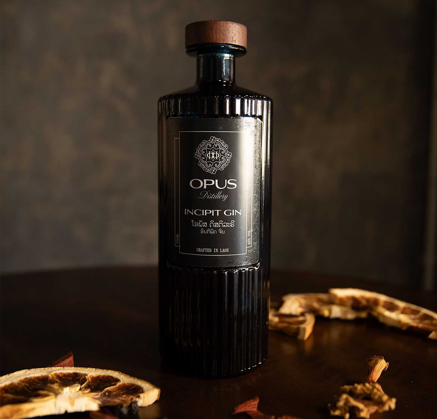 Opus Distillery Incipit Gin bottle crafted in Laos surrounded by dried citrus slices and botanicals on a dark background
