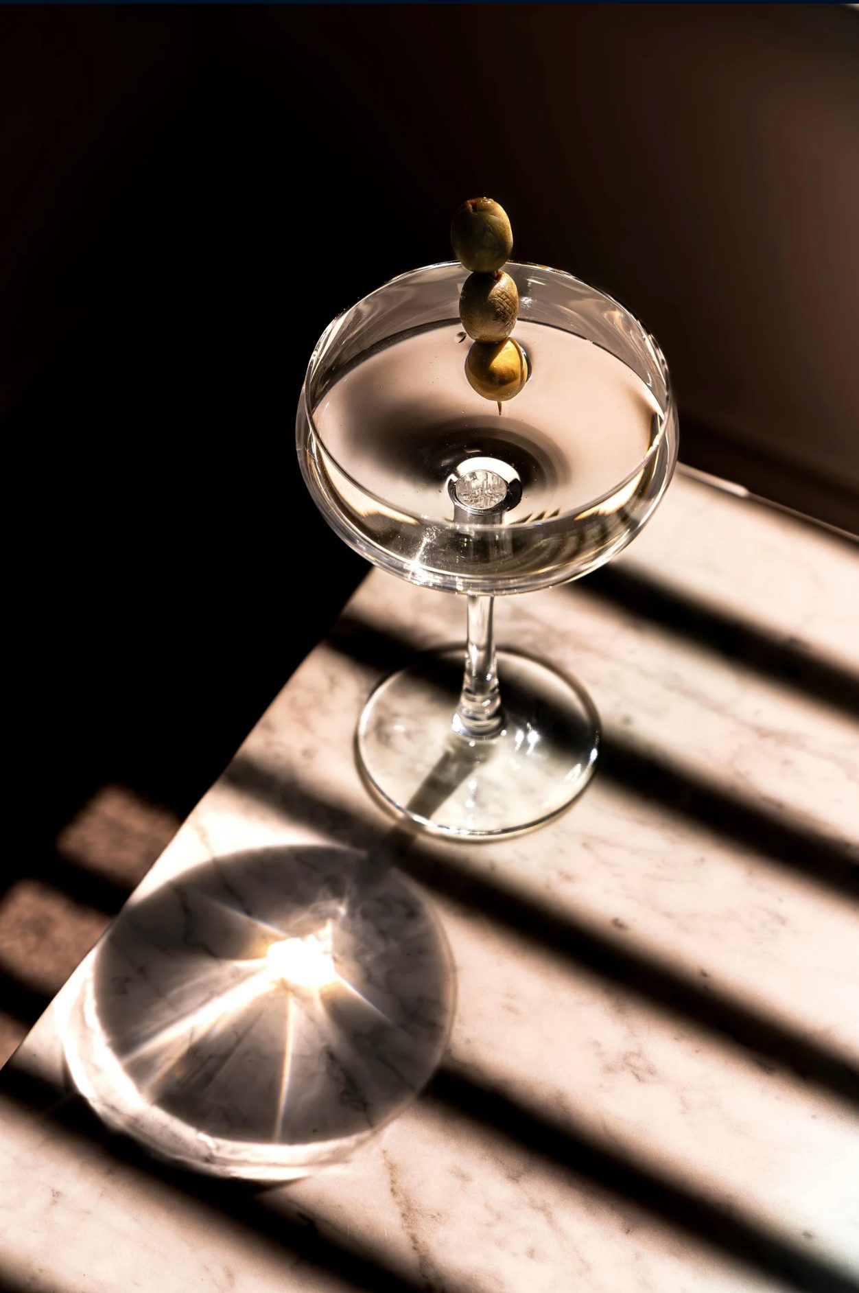 Opus Gin martini in a coupe glass garnished with olives on a marble surface